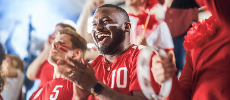 Homem sorrindo junto a torcida de futebol