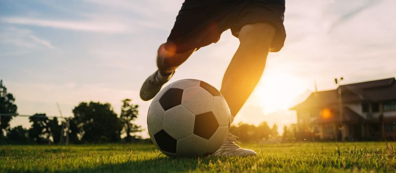 Jogador de futebol chutando bola com pôr do sol ao fundo